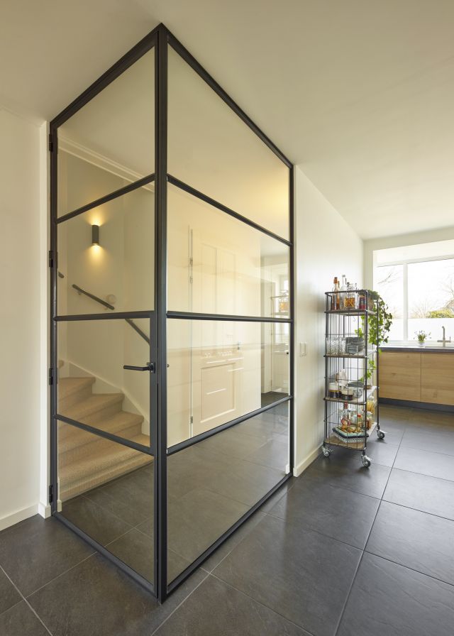 Transparante scheiding tussen woonkamer en hal door hoekwand van staal en glas. Project in Voorhout.