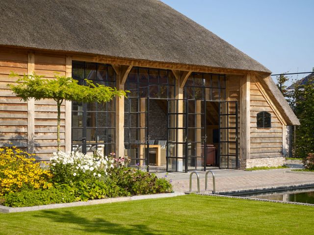 Openslaande stalen deuren in een bijgebouw van eikenhout geven toegang tot het terras in Werkhoven.